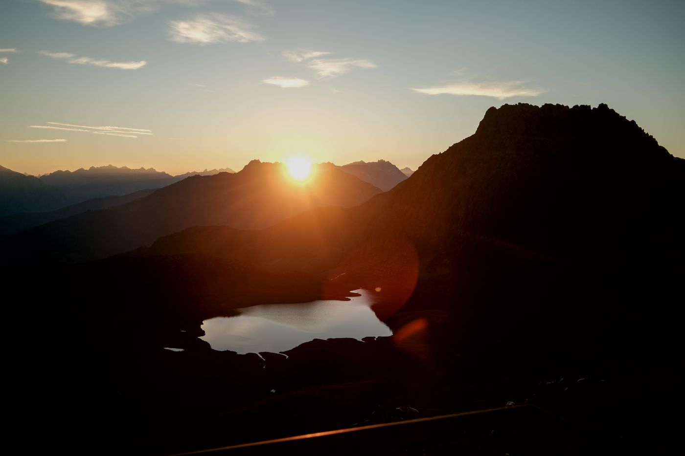 Sonnenaufgang über den Bergen, darunter ein Bergsee