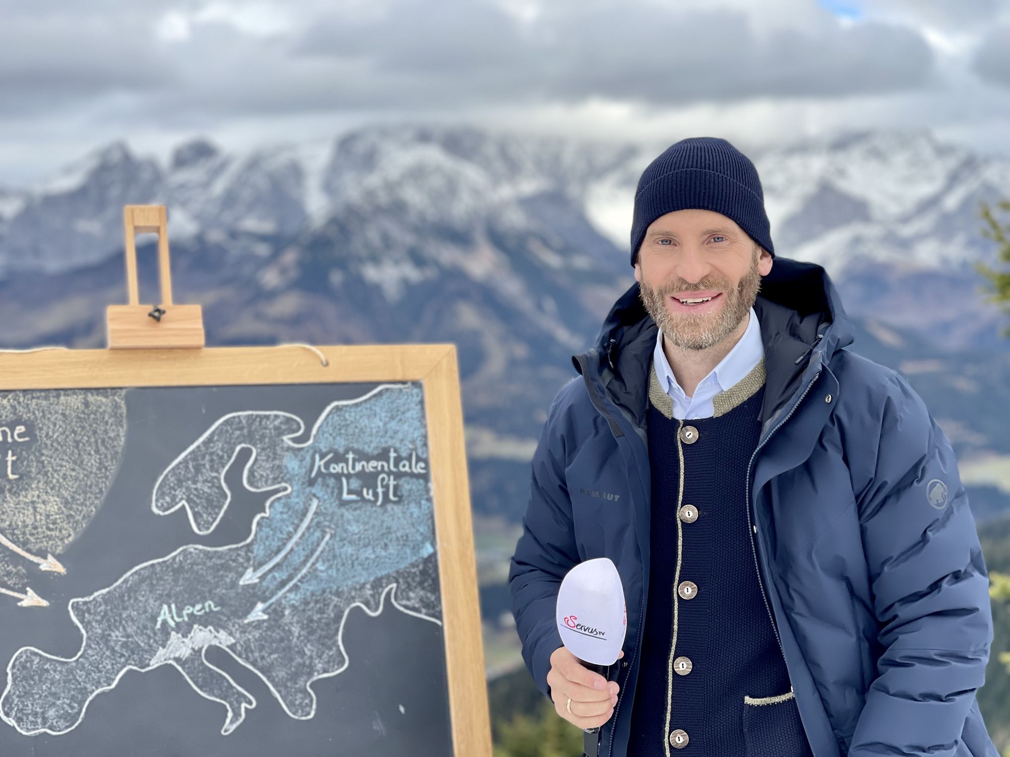 Sebastian Weber an der Wettertafel vor verschneiten Bergen